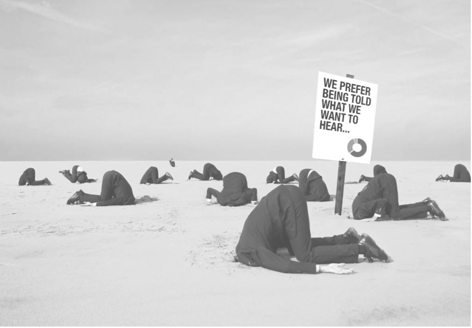 Image of multiple people in suits with their heads buried and a sign saying 'We prefer being told what we want to hear'